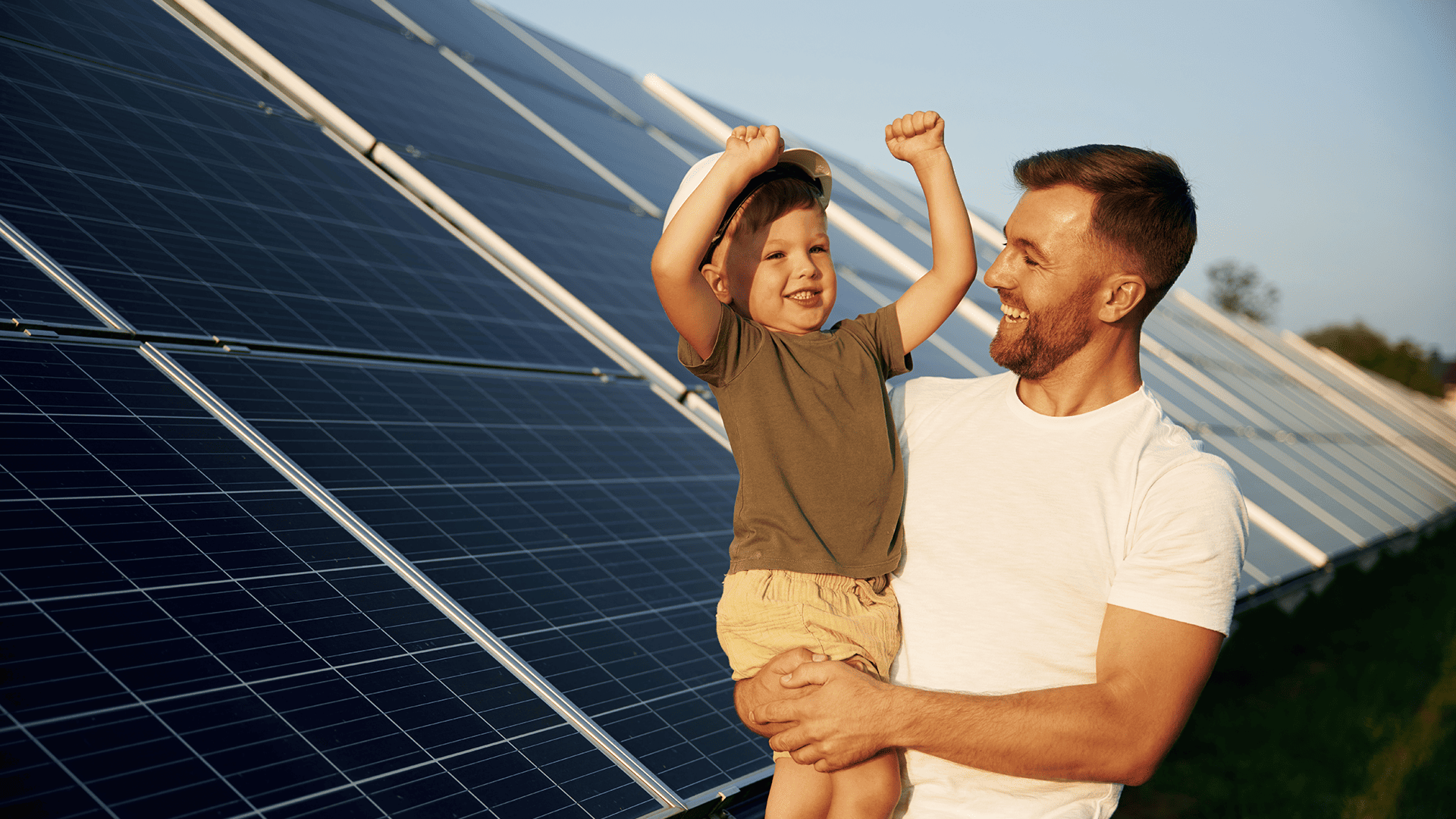 Eine Solaranlage im Hintergrund. Vorne steht Vater und hält seinen Sohn auf den Armen.